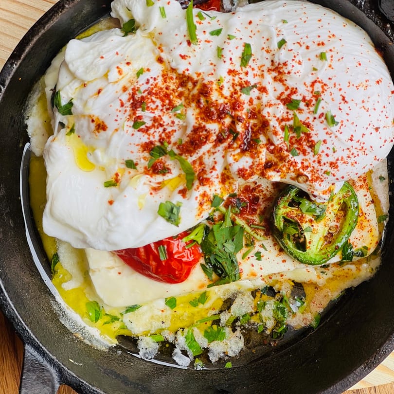 Creamy white cheese dish with red peppers, green jalapeños, and herbs in a cast iron skillet.