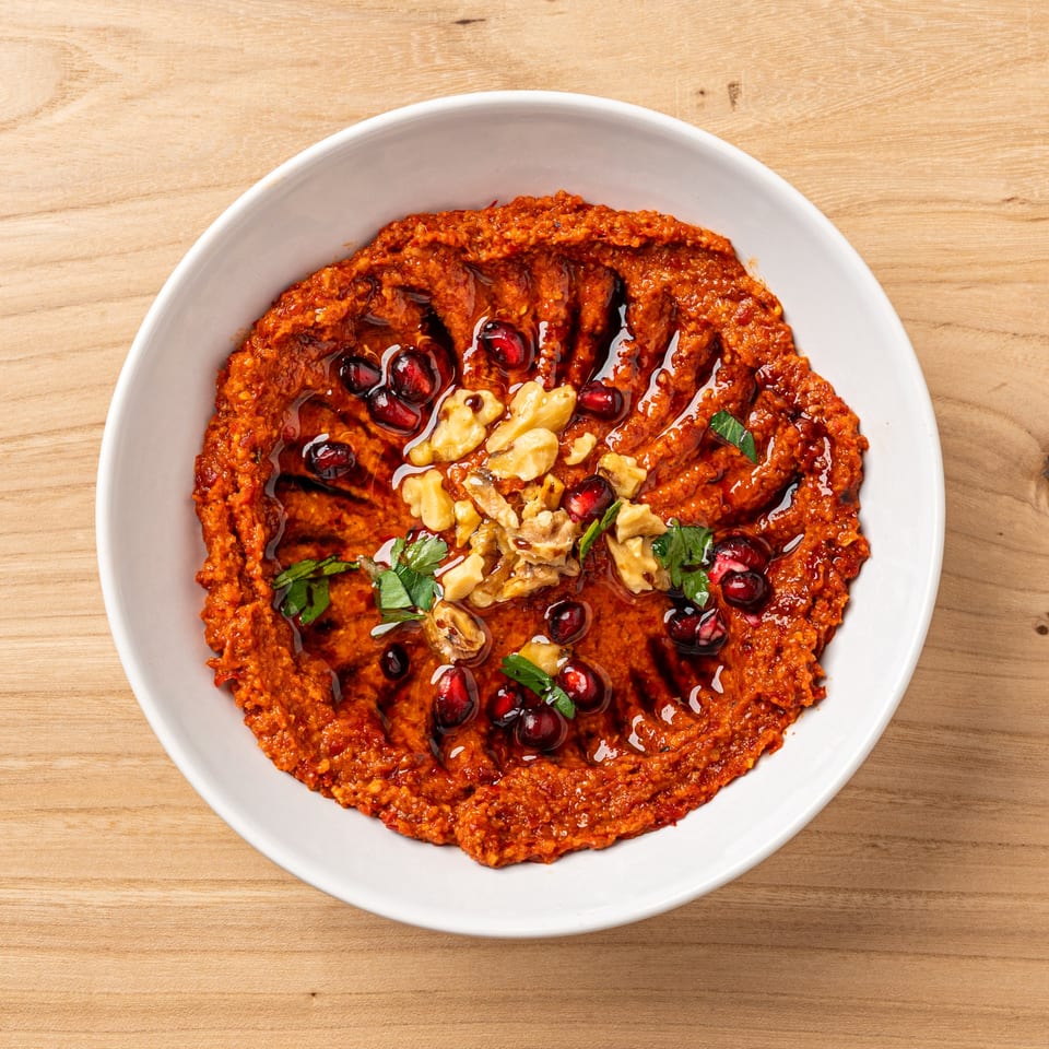 Nour's Muhammara, a vibrant red dip garnished with walnuts, pomegranate seeds, and parsley.
