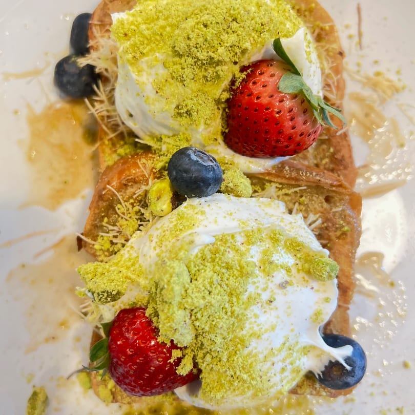 Golden pastry topped with two cream scoops, pistachio, strawberries, blueberries, and syrup.